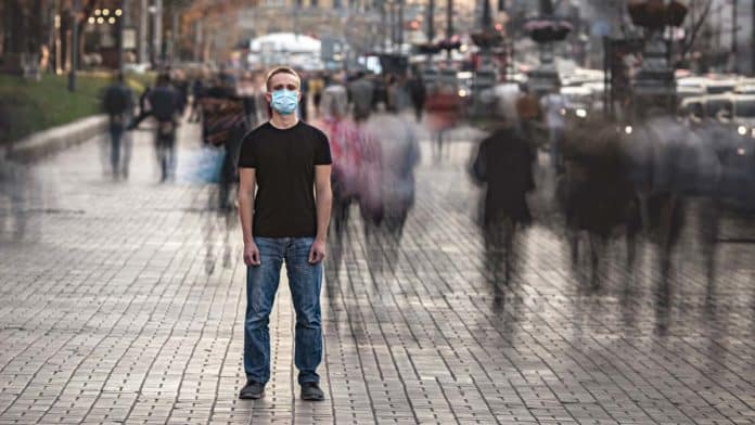 The young man with medical face mask stands on the crowded stree